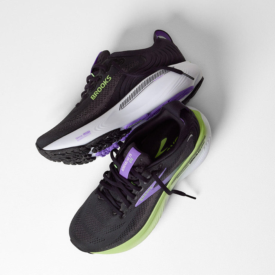 A pair of Brooks running shoes in black with purple and neon green accents, displayed on a light gray background.