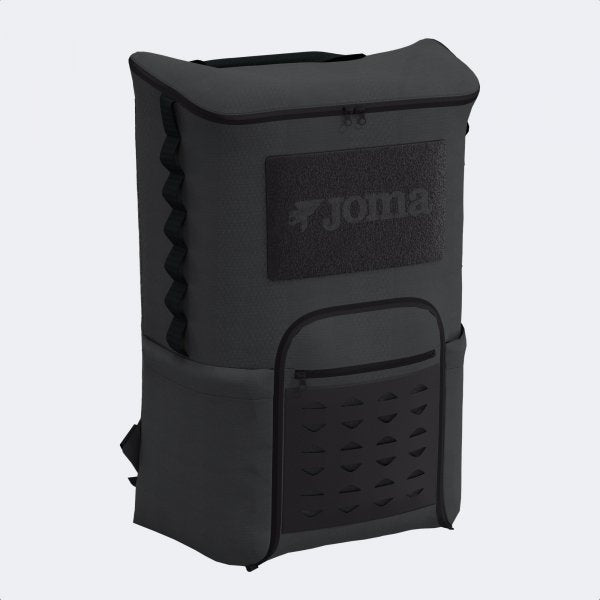 A black Joma backpack shown from a three-quarter angle against a light gray background. The backpack features a textured front panel with a large Joma logo patch, a front zippered pocket with a vented pattern, and side compression straps.