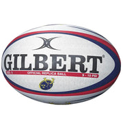 A Gilbert rugby ball with a white textured surface, featuring navy blue and red stripes, the black Gilbert brand name, and a small gold and blue club crest, photographed on a clean white background.