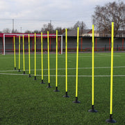 Yellow training poles on a football field with a goalpost in the background.