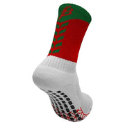 A single athletic sock shown on a light gray background. The sock features a white ribbed cuff and foot, black grip dots on the sole, a red and green upper section with green chevron-like stripes, and a green cuff with a red logo.