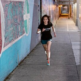 Woman running on a sidewalk next to a colorful mural.